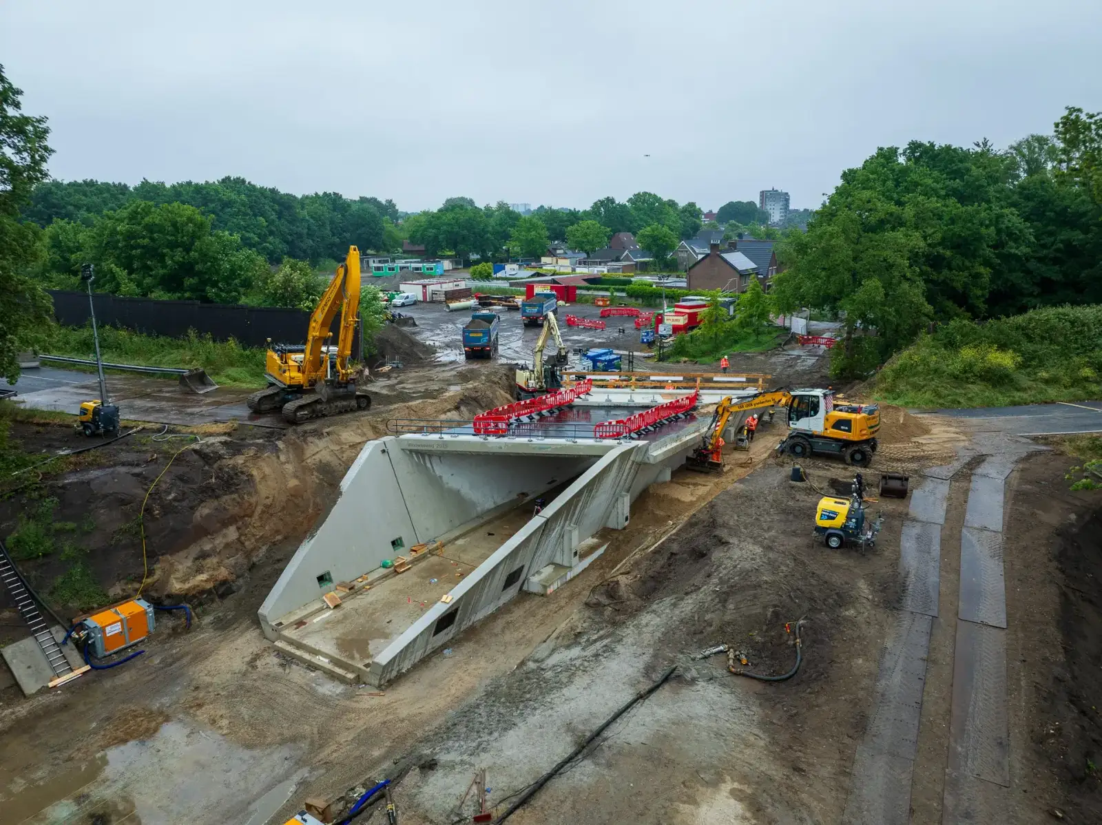 Bouw van een betonnen onderdoorgang met graafmachines naast een woonwijk