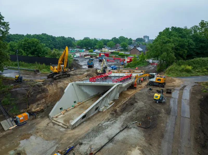 Bouw van een betonnen onderdoorgang met graafmachines naast een woonwijk