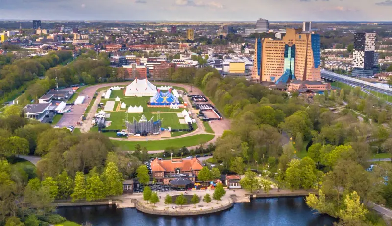 Park met festivaltenten, een vijver en hoogbouw op de achtergrond